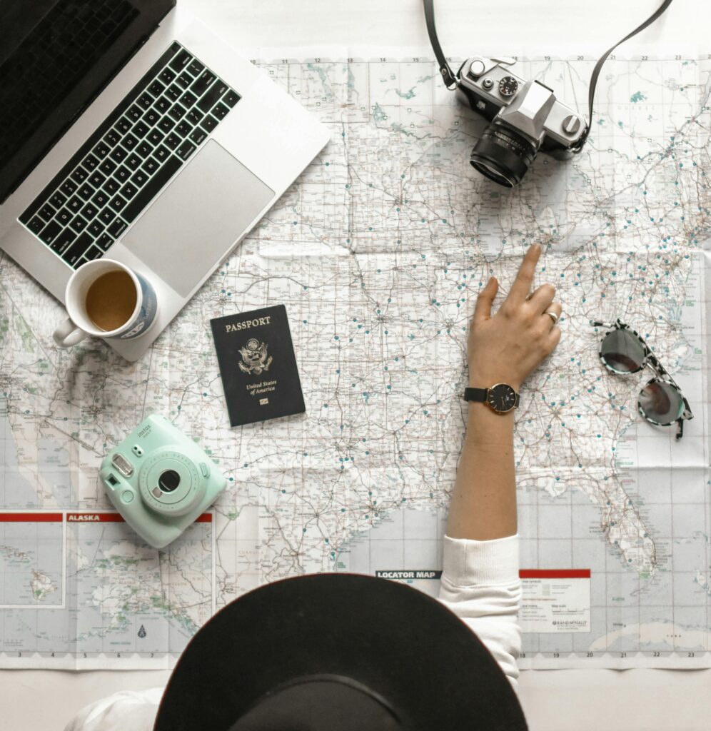 Delhi Tour Package Hand on map with camera, passport, laptop, and coffee, perfect for travel planning inspiration.
