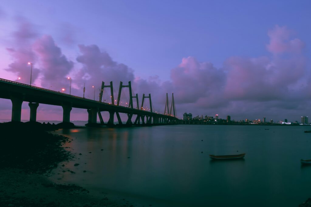 A stunning twilight photograph of an architectural bridge over calm waters, with a vibrant city skyline visible in the background.