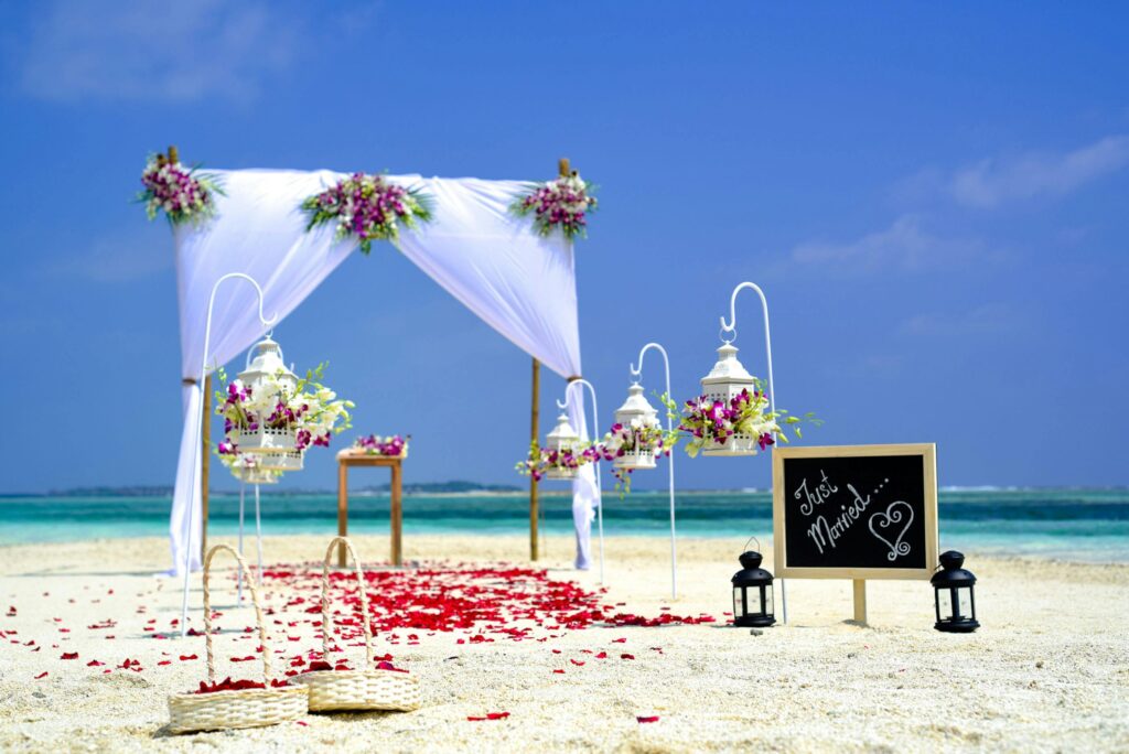 Stunning beach wedding arrangement with floral decor and lanterns on a sunny day.