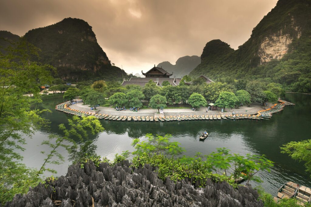 A scenic view of an island with boats, temple, and lush greenery in a tranquil setting.