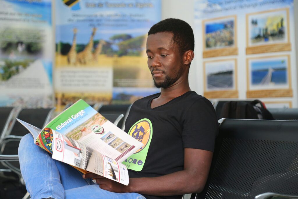 A man sits indoors reading a brochure about Olduvai Gorge, in a modern waiting area.